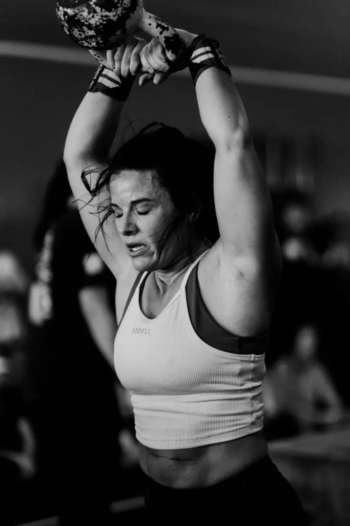 Athlète réalisant un mouvement avec un kettlebell au-dessus de la tête pendant un entraînement intensif.