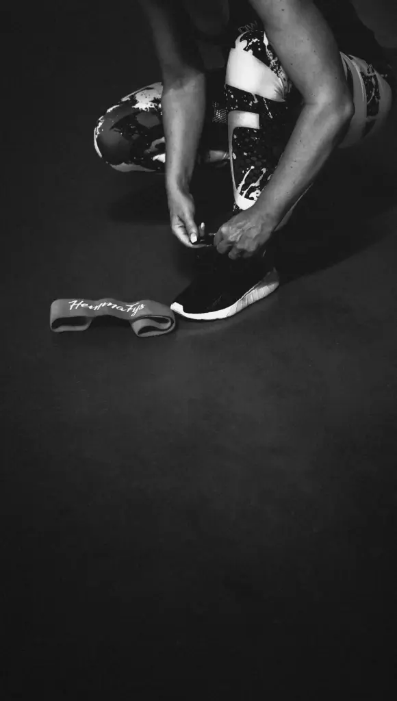 Athlète attachant ses chaussures de sport au sol avant de commencer un entraînement, avec une bande de résistance à proximité.