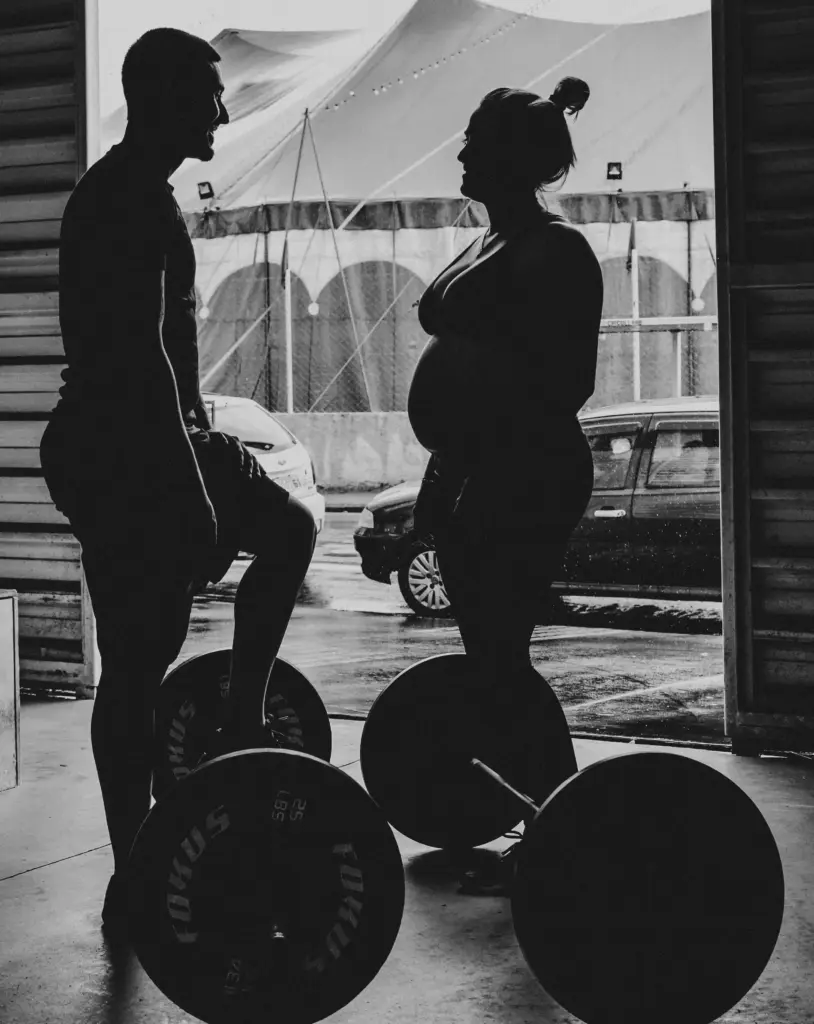 Deux athlètes échangeant avant un entraînement de musculation, avec des barres chargées au premier plan.